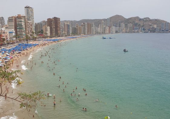 Crowded Levante beach in Benidorm under a July sun, skyline behind