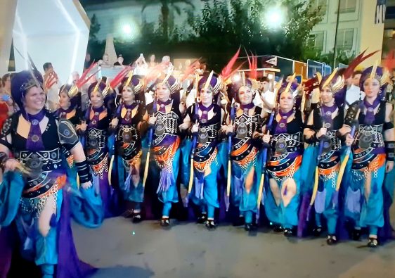 A filà in teal and purple costume marching in the Moros y Cristianos parade in Benidorm