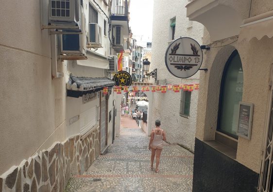 A narrow cobbled alley in Benidorm Old Town, bunting overhead and a woman walking away from the camera