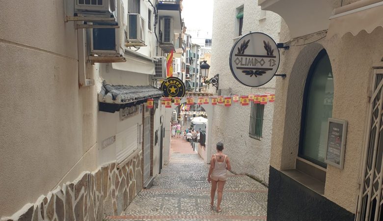 A narrow cobbled alley in Benidorm Old Town, bunting overhead and a woman walking away from the camera