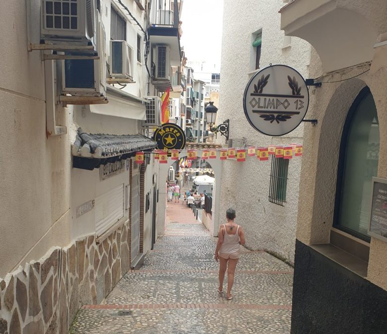 A narrow cobbled alley in Benidorm Old Town, bunting overhead and a woman walking away from the camera